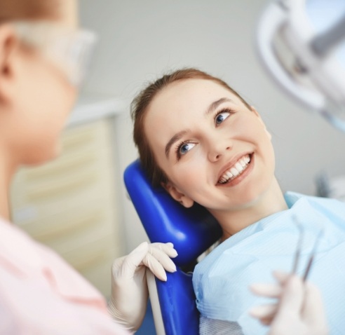 Young woman leaning back in dental chair and smiling at her dentist