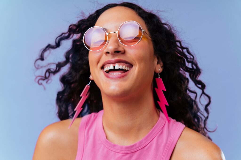 Woman in pink tank top with lightning earrings smiling with diastema